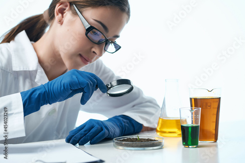 Woman in white coat examines plants microbiology