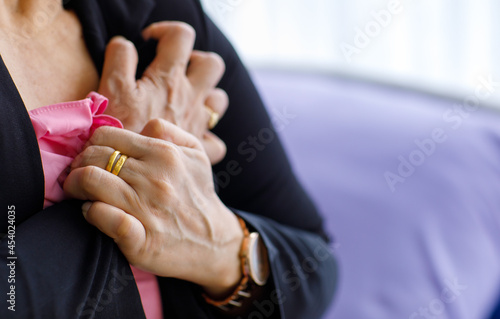 Unidentified woman sitting on bed suffering from sudden heart attack and hold chest. Concept of emergency health care and affected from  Cardiopulmonary Resuscitation, heart problem