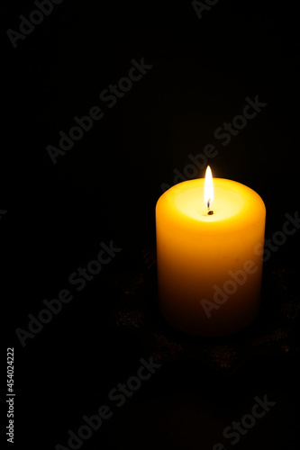 A large candle burns in complete darkness.