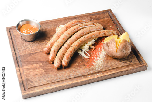Stack of cooked sausages served on a rustic wooden board with sauce and baked potatoes.