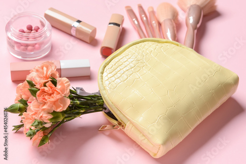 Stylish bag, decorative cosmetics and flowers on color background, closeup