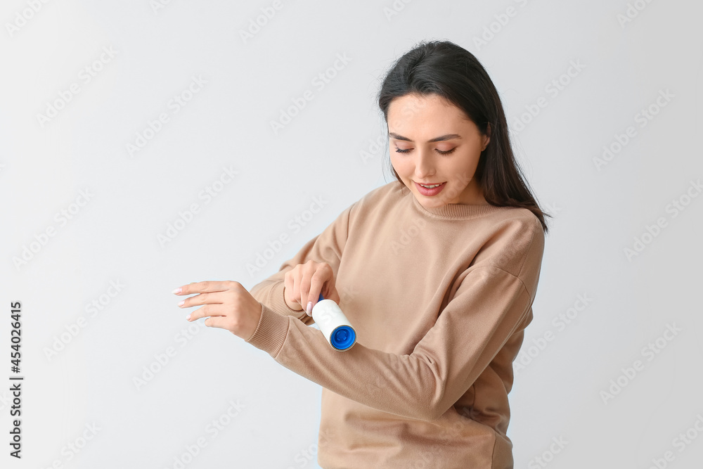 Young woman cleaning her sweatshirt with lint roller on light background Young woman cleaning her sweatshirt with lint roller on light background