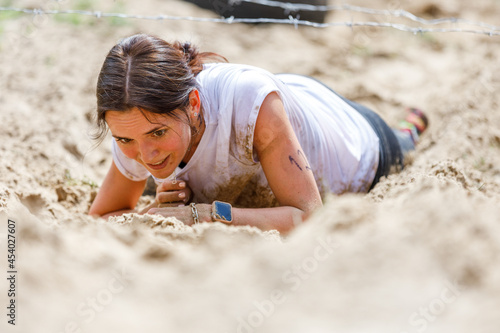 Young sportswoman crawling under barbed wire on her obstacle race course