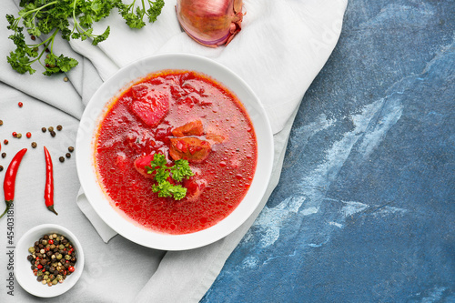 Bowl with tasty borscht, onion, parsley and peppercorns on color background