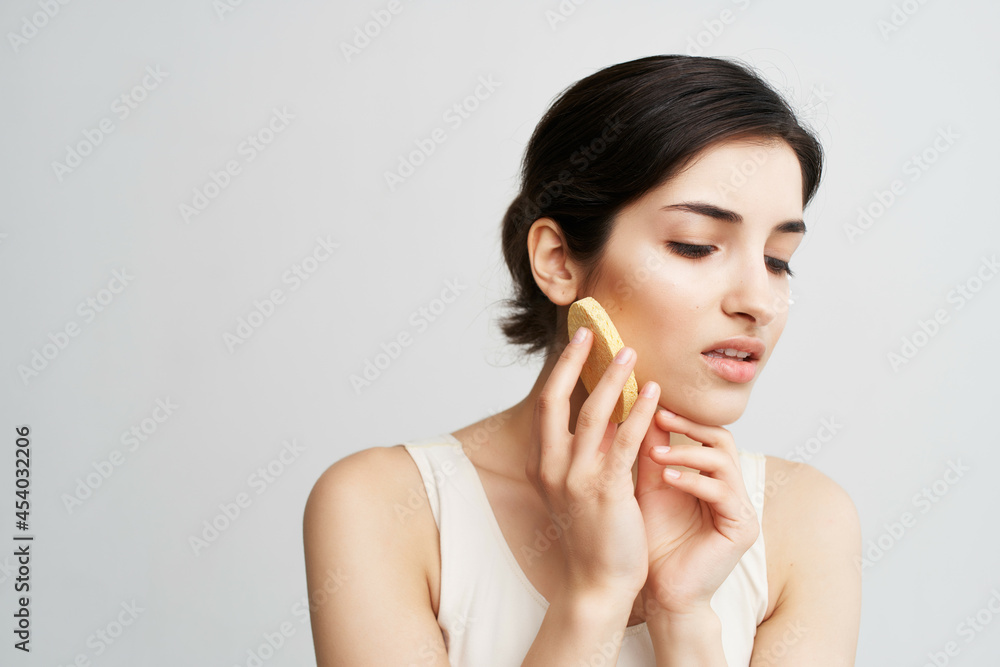 pretty brunette in a white tank top apply cream with a sponge on her face pretty brunette in a white tank top apply cream with a sponge on her face