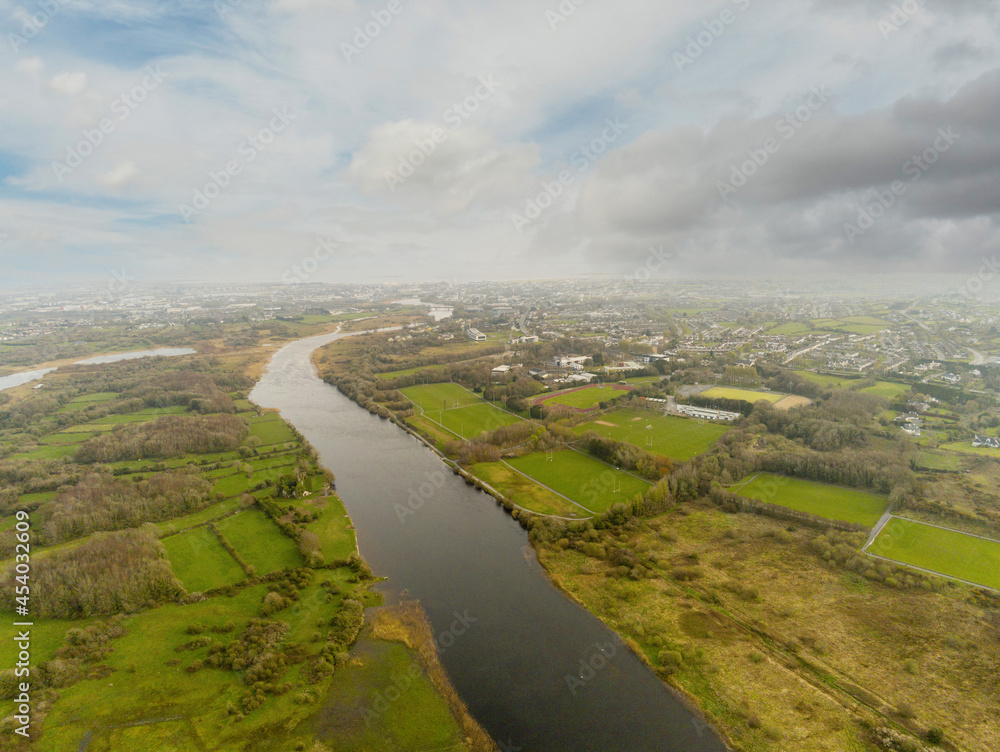 Aerial drone view on river Corrib, Galway city, Ireland. Park and sports ground for Irish National sports hurling, camogie, rugby on the right. Cloudy sky