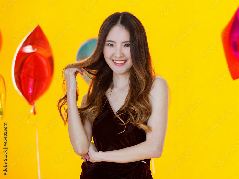 Asian young sexy beautiful long hair girl in dress standing smiling posing happily in front of colorful star and round shape helium air balloons on yellow background in surprise party Asian young sexy beautiful long hair girl in dress standing smiling posing happily in front of colorful star and round shape helium air balloons on yellow background in surprise party