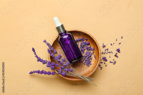 Bowl with bottle of lavender essential oil and flowers on color background photo