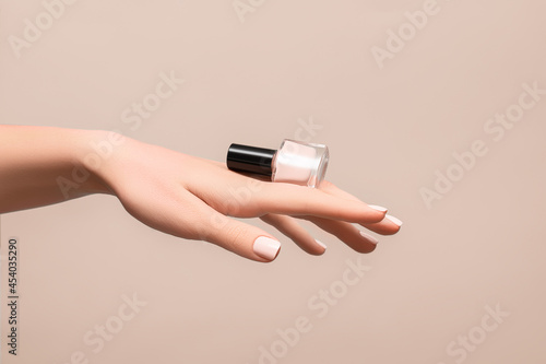 Female hand with pink nail design. Pink fingernails manicure. Woman hand hold pink nail polish on beige background photo
