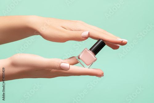 Female hands with pink nail design. Pink fingernails manicure. Woman hands hold pink nail polish on green background