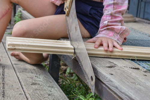 the child girl with a hacksaw saws a board outside photo without processing