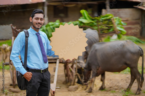 Young indian animal husbandry officer or agronomist showing board with copy space at cattle farm