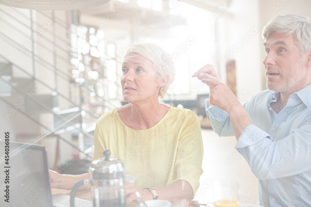 Older couple laughing together at breakfast table with laptop Older couple laughing together at breakfast table with laptop