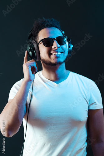 Smile Young African American man portrait wearing headphones and enjoy music over black Background. Blue light reflection on face.