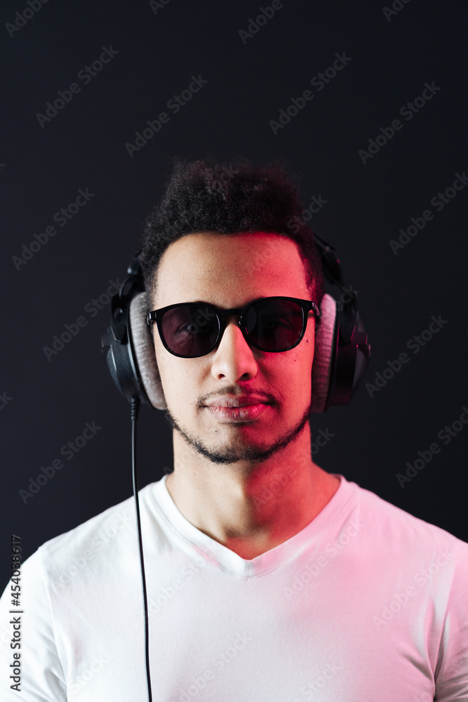 Smile Young African American man portrait wearing headphones and enjoy music over black Background. Red light reflection on face. Smile Young African American man portrait wearing headphones and enjoy music over black Background. Red light reflection on face.