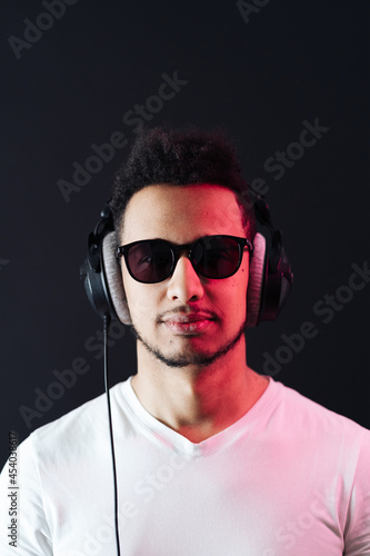 Smile Young African American man portrait wearing headphones and enjoy music over black Background. Red light reflection on face.