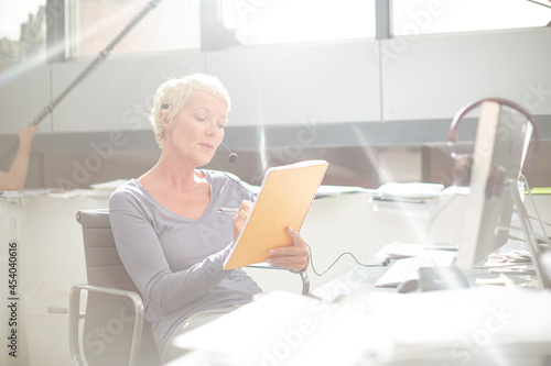 Businesswoman in headset writing on notepad in office
