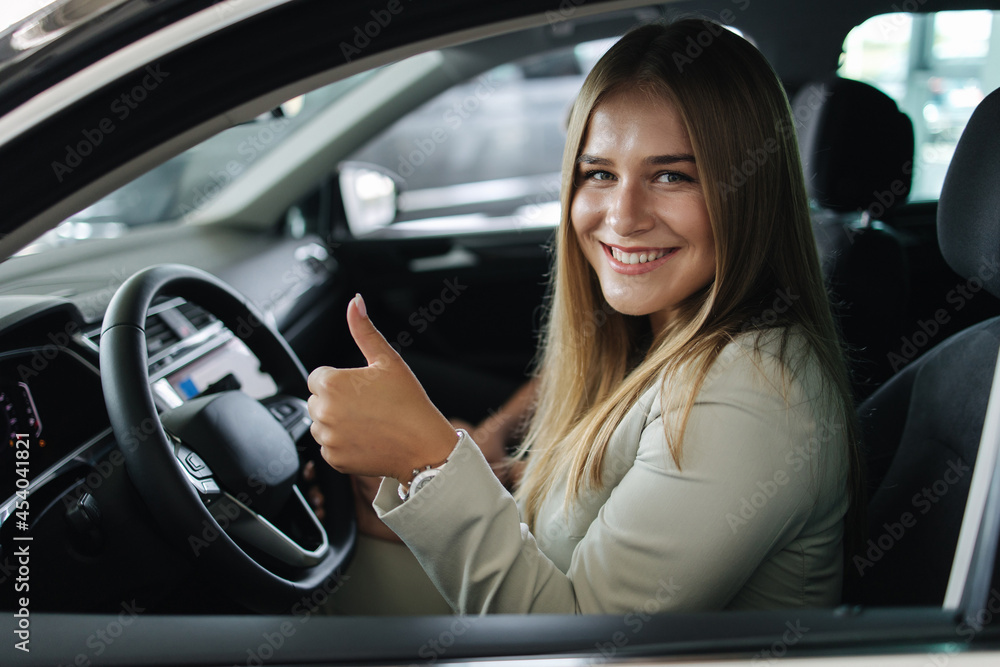 Attactive young bussines woman sitting in car in car showroom. Woman choosing new car. Beautiful blond hair female in suit