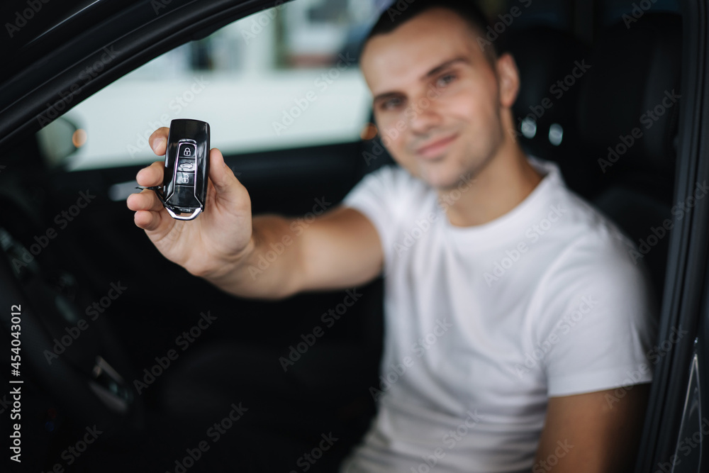 Man sitting in his new car in car showroom. Portrait of handsome man in car hold keys in hands. Keys in focus Man sitting in his new car in car showroom. Portrait of handsome man in car hold keys in hands. Keys in focus
