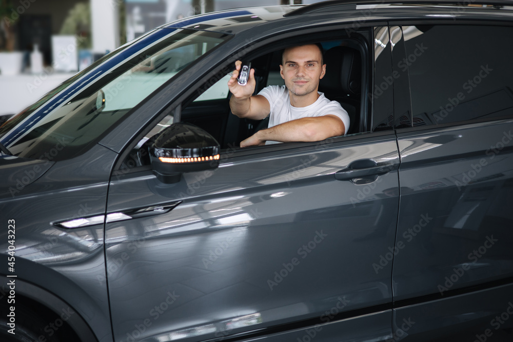 Man sitting in his new car in car showroom. Portrait of handsome man in car hold keys in hands