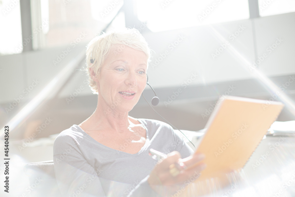 Businesswoman in headset writing on notepad in office Businesswoman in headset writing on notepad in office