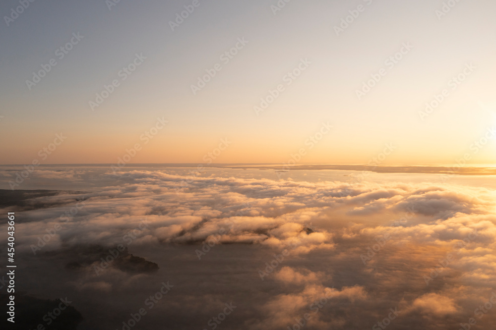 Fototapeta premium Aerial top view gold sunrise over clouds in blue sky. Aerial top view cloudscape. Texture of clouds. View from above. Orange sunrise or sunset over clouds. Panorama clouds texture