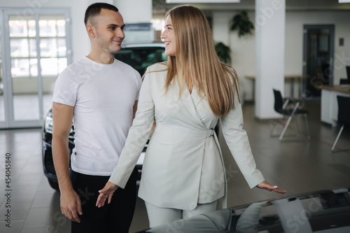 Happy woman hug his husband afrer buying car in car showroom. Man and woman buy new car photo