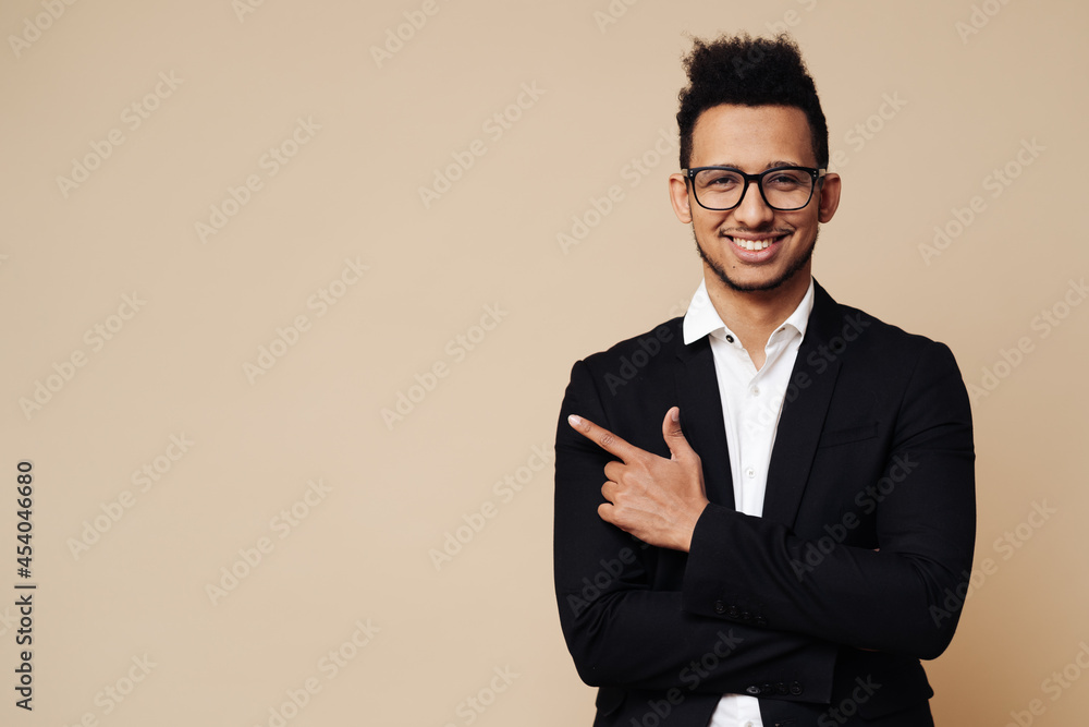 Portrait of handsome young smiling Afro man wearing glasses smiling and standing with open hand gesture isolated on beige background with copy space Portrait of handsome young smiling Afro man wearing glasses smiling and standing with open hand gesture isolated on beige background with copy space