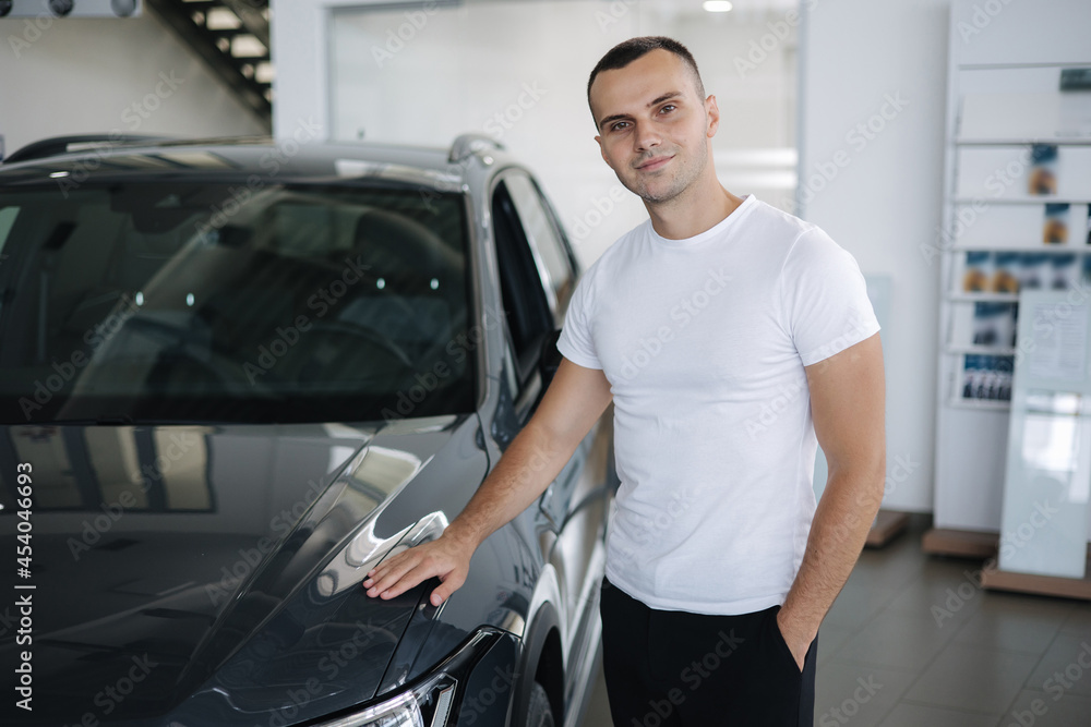 Portrait of handsome man standing by car in car shoowroom. Man buying new car Portrait of handsome man standing by car in car shoowroom. Man buying new car