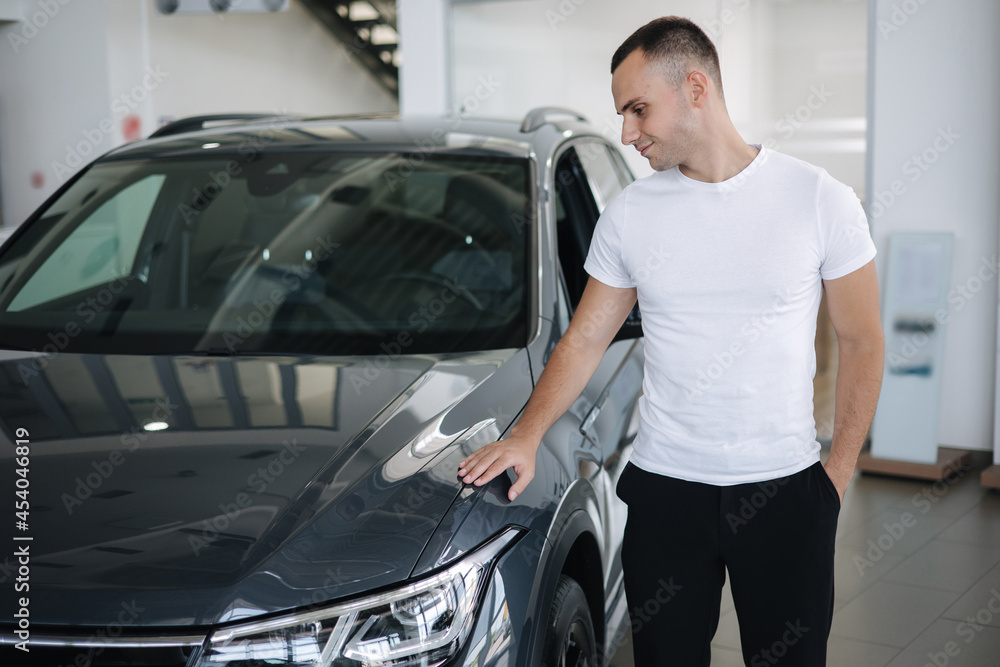 Portrait of handsome man standing by car in car shoowroom. Man buying new car Portrait of handsome man standing by car in car shoowroom. Man buying new car