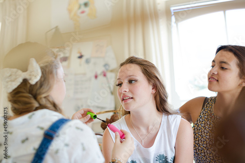 Three teenage girls doing make-up and brushing hair in bedroom
