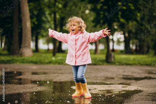 Cute little girl jumping into puddle in a rainy weather