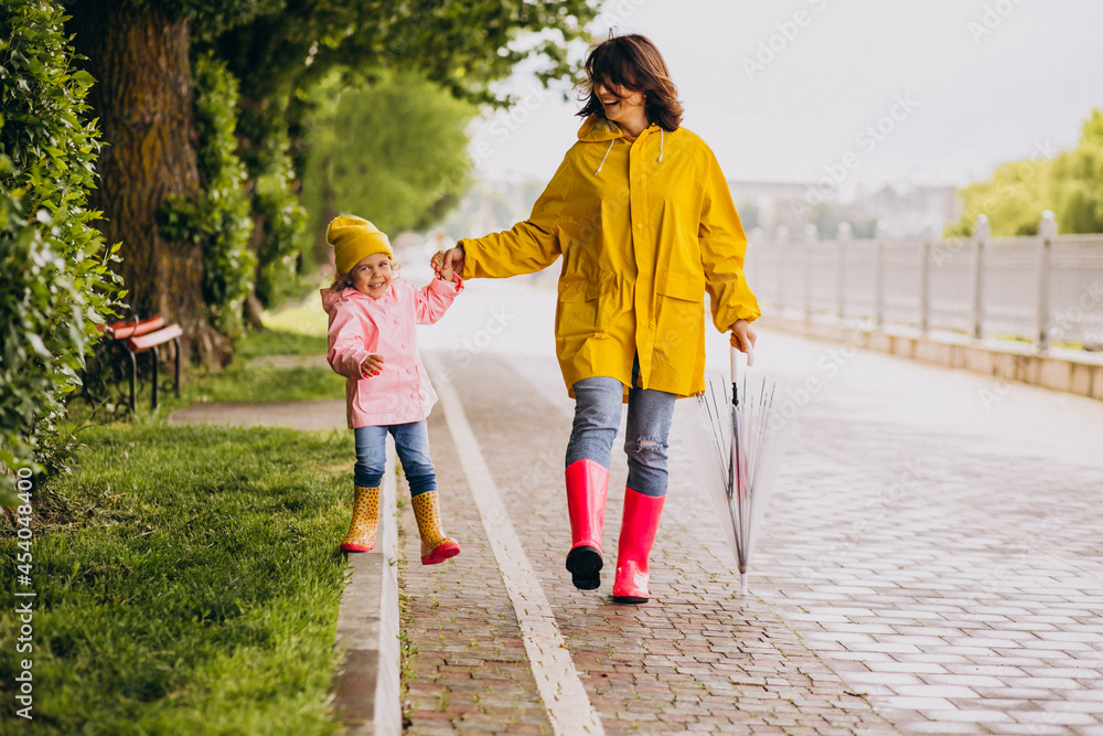 Mother with daughter walking in park in the rain wearing rubber boots Mother with daughter walking in park in the rain wearing rubber boots