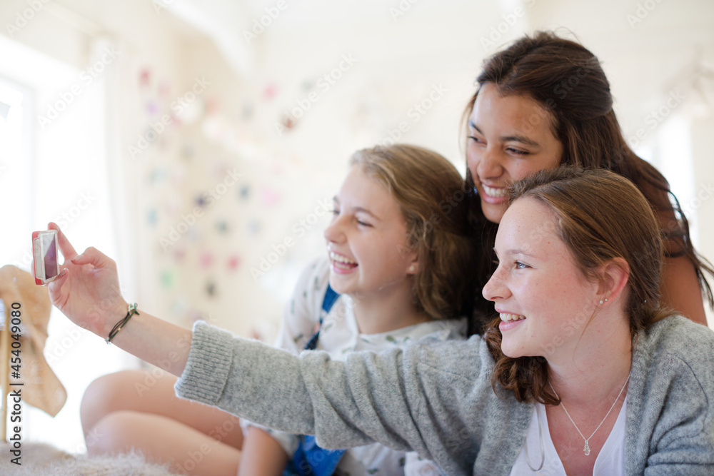 Three teenage girls taking selfie while lying on bed in bedroom