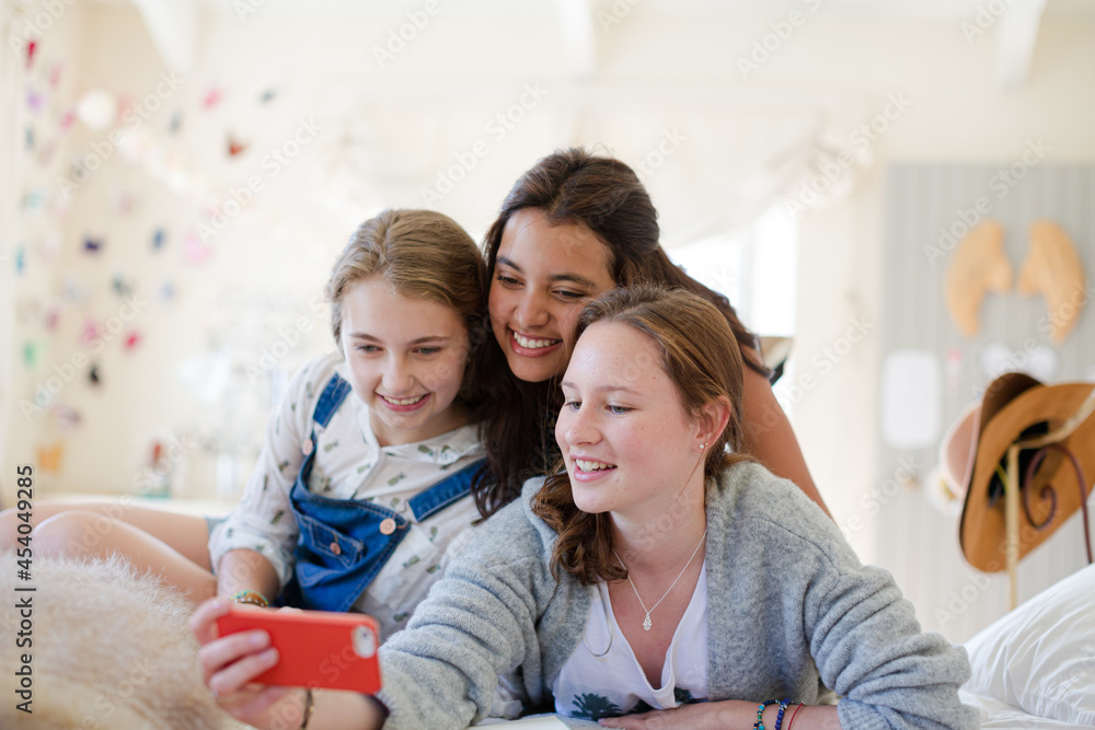 Three teenage girls using smart phone together while lying on bed Three teenage girls using smart phone together while lying on bed