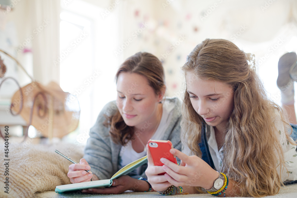 Two teenage girls on bed writing in notepads Two teenage girls on bed writing in notepads