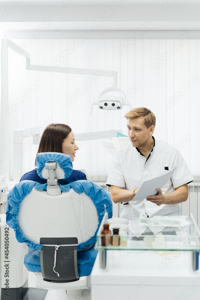 Obraz premium Male Professional Dentist With Gloves And Mask Holding papers photo And Show What The Treatment Will Look Like Of The Patient's Teeth. Discussion Of The Treatment Plan And Healthy Smile