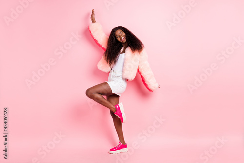 Full size photo of excited pretty dark skin lady look empty space have fun dancing isolated on pink color background