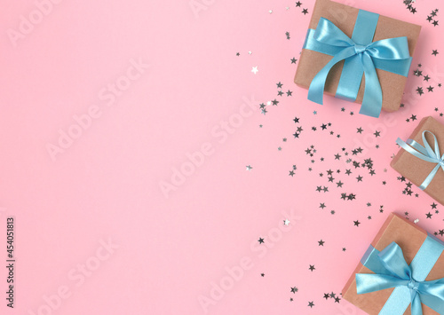 Frame made of gift boxes with blue  ribbons and silver confetti on a pink pastel background.