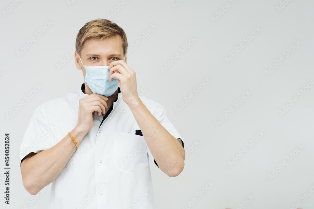 Portrait of a young male medical doctor putting sterile mask isolated on white background with copy space Portrait of a young male medical doctor putting sterile mask isolated on white background with copy space