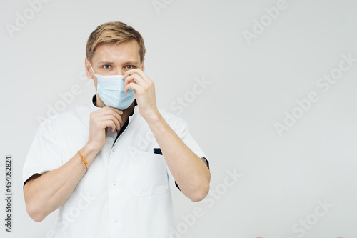 Portrait of a young male medical doctor putting sterile mask isolated on white background with copy space