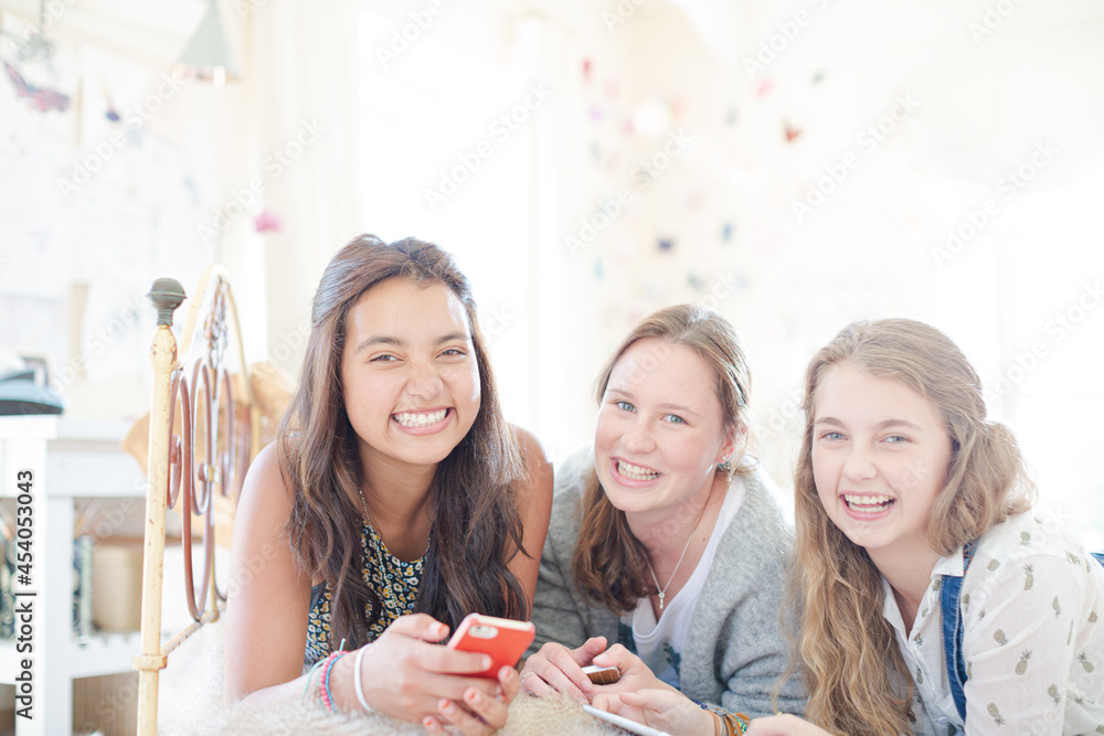 Three teenage girls using smart phone together while lying on bed in bedroom Three teenage girls using smart phone together while lying on bed in bedroom