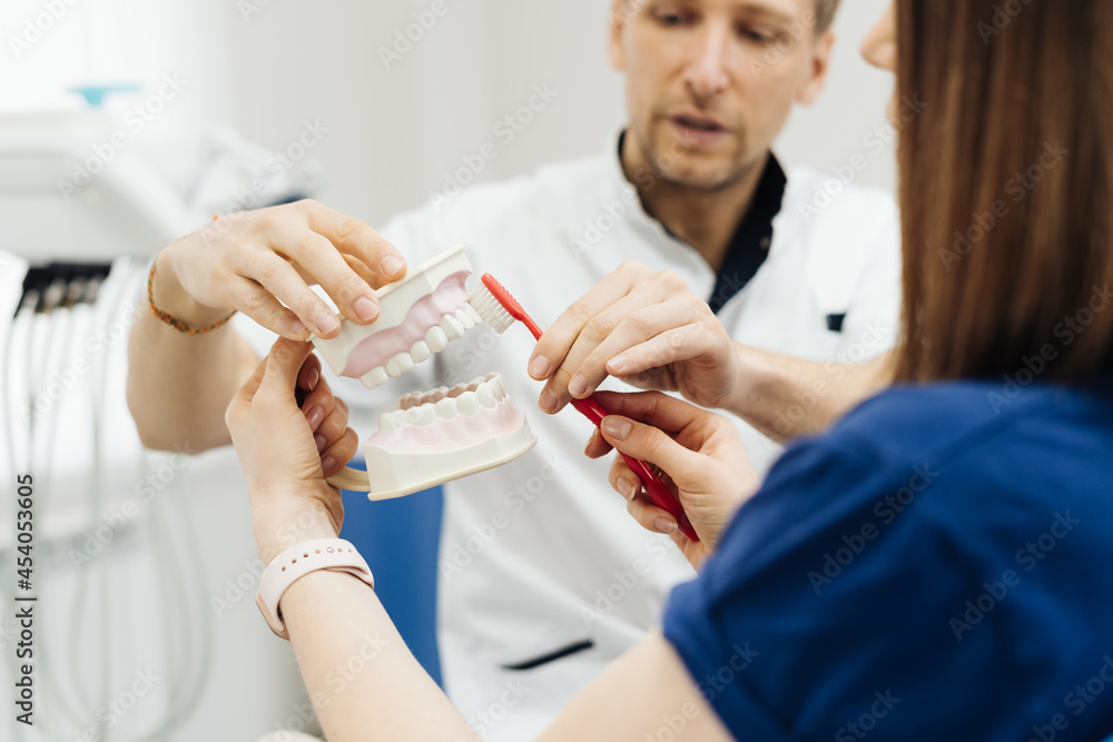 Dentist showing the correct dental hygiene using mock-up of skeleton of teeth. Stomatologist doctor explaining proper dental hygiene to patient holding sample of human jaw with toothbrush. Dentist showing the correct dental hygiene using mock-up of skeleton of teeth. Stomatologist doctor explaining proper dental hygiene to patient holding sample of human jaw with toothbrush.