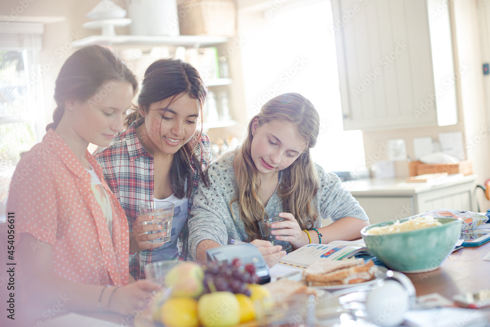 Teenage girls learning at table in kitchen