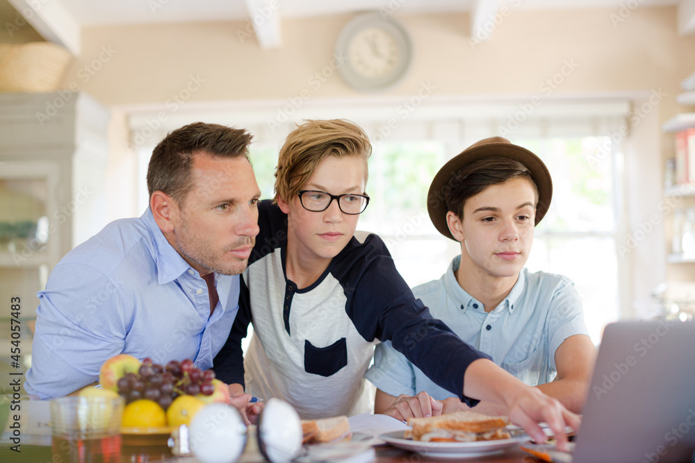 Teenage boys with father using laptop in dining room