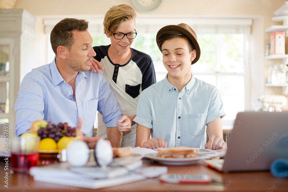 Teenage boys with father using laptop in dining room Teenage boys with father using laptop in dining room