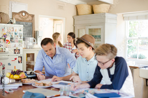 Teenagers with mid adult man sitting at table in dining room