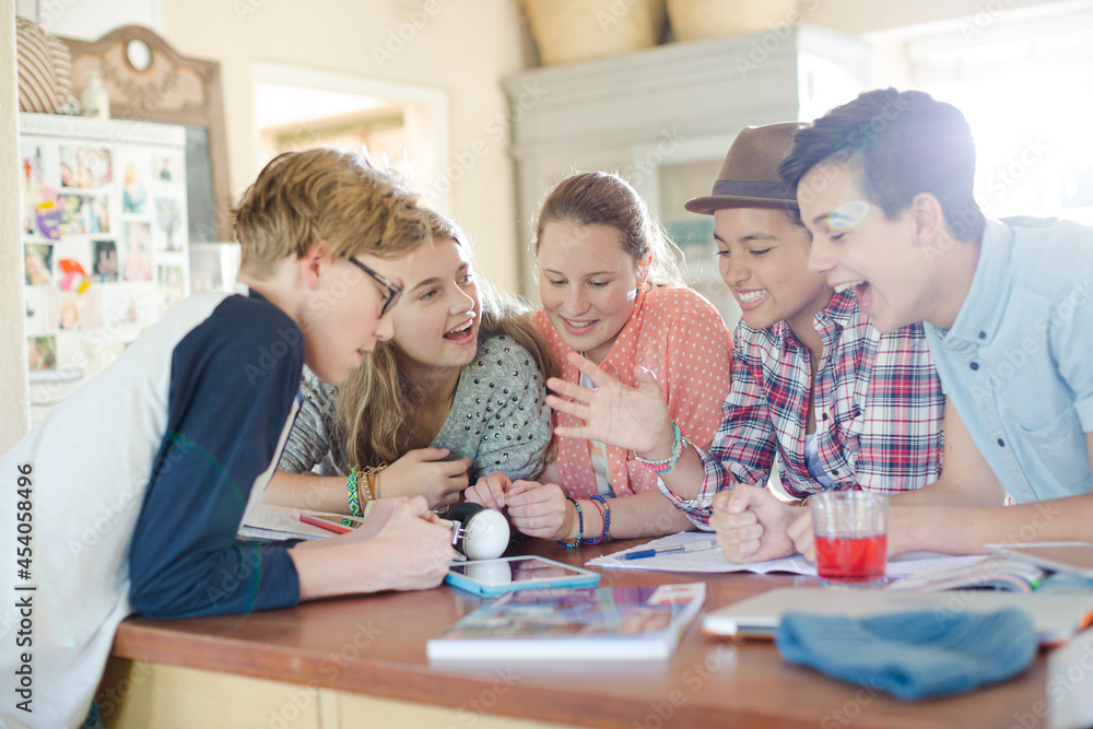 Group of teenagers using together digital tablet at table in kitchen Group of teenagers using together digital tablet at table in kitchen