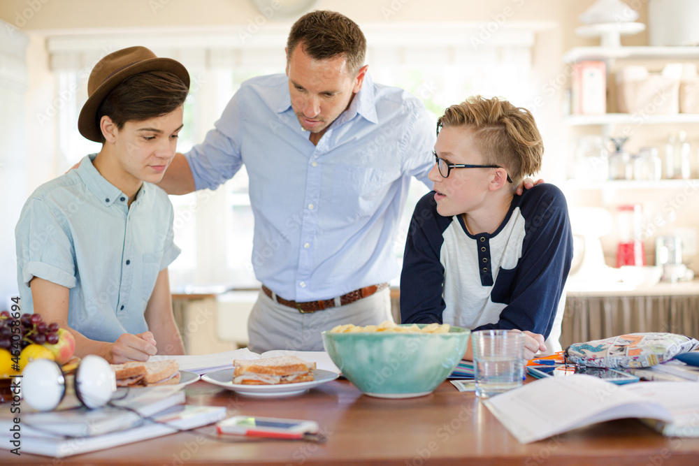 Teenage boys with father using laptop in dining room Teenage boys with father using laptop in dining room