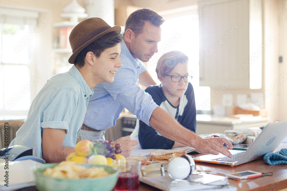 Teenage boys with father using laptop in dining room Teenage boys with father using laptop in dining room
